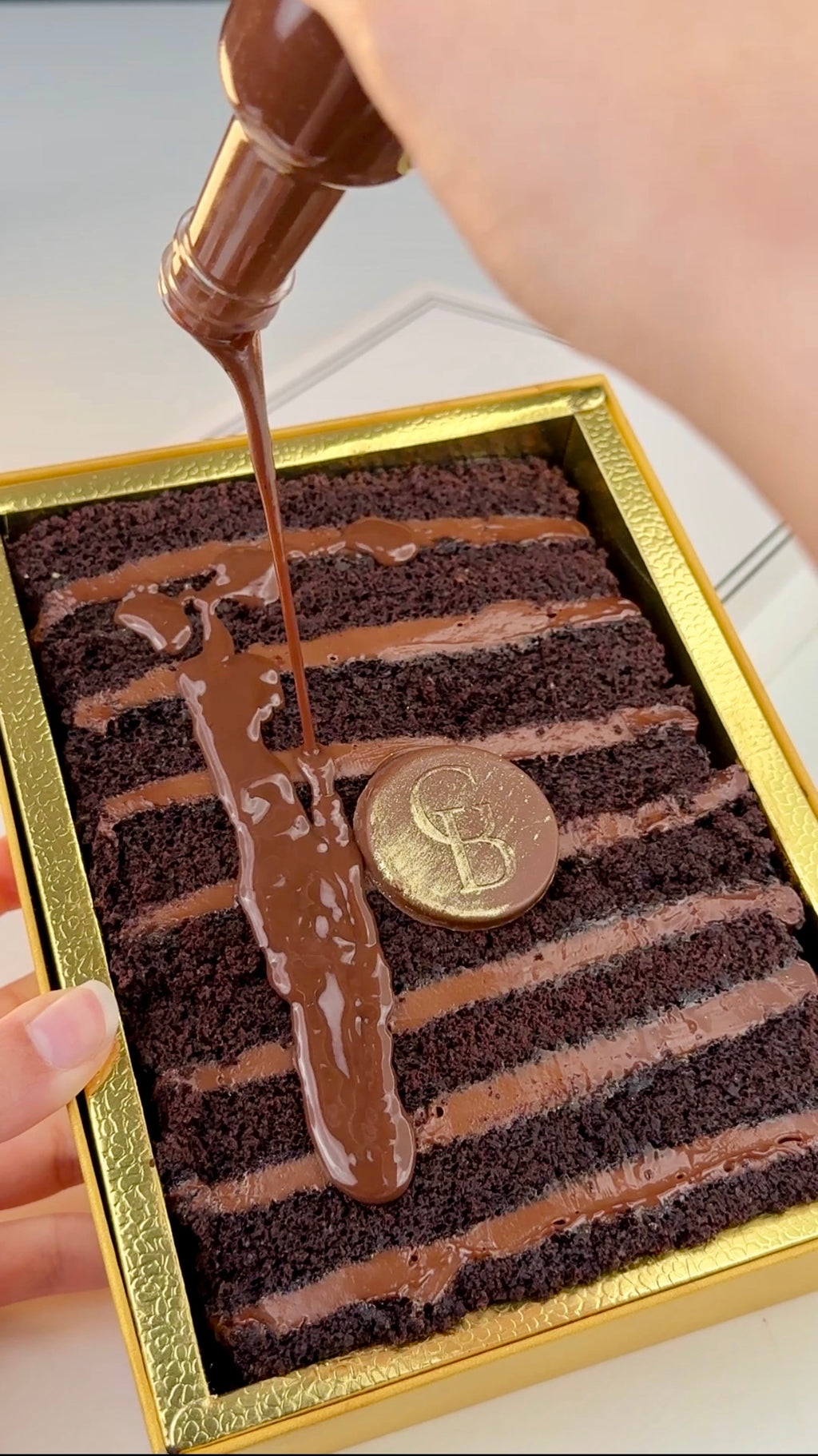 Chocolate ShortStack with a GB coin in a decorative box, with chocolate sauce being poured over it.